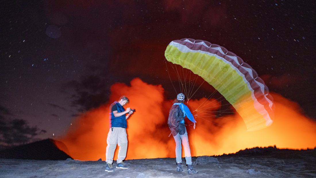 Filming beside a paraglider launching in front of the glowing volcano crater at night
