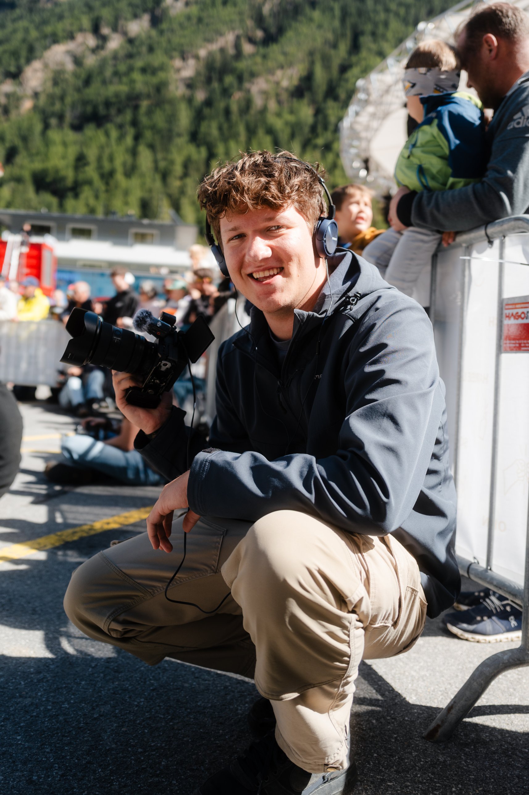 Gabriel crouching trackside with a camera and headphones at an alpine event