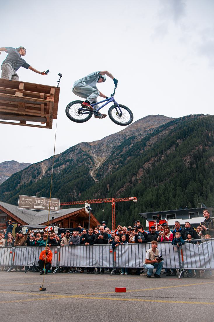 BMX rider jumping high over a crowd in an alpine village